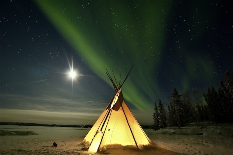 Tipi iluminado bajo una aurora boreal verde en el norte de Canadá